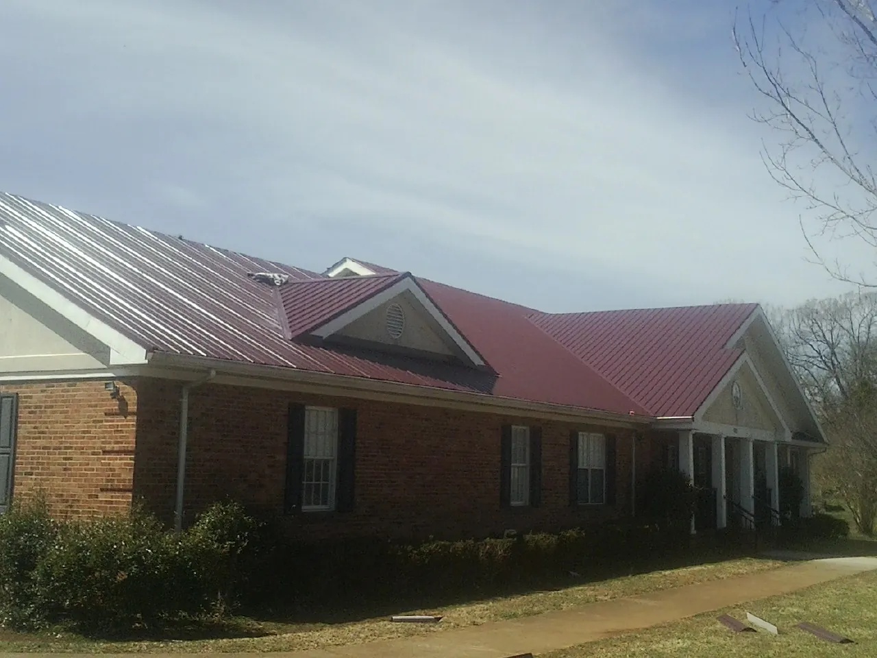 Red metal roof with gabled entries on a long brick building, from a Hail Damage Roof Repair job in Seneca
