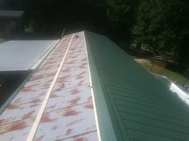 Old rusted panels beside newly installed green metal roofing — Wind Damage Roof Repair by Roofing Brothers in Seneca